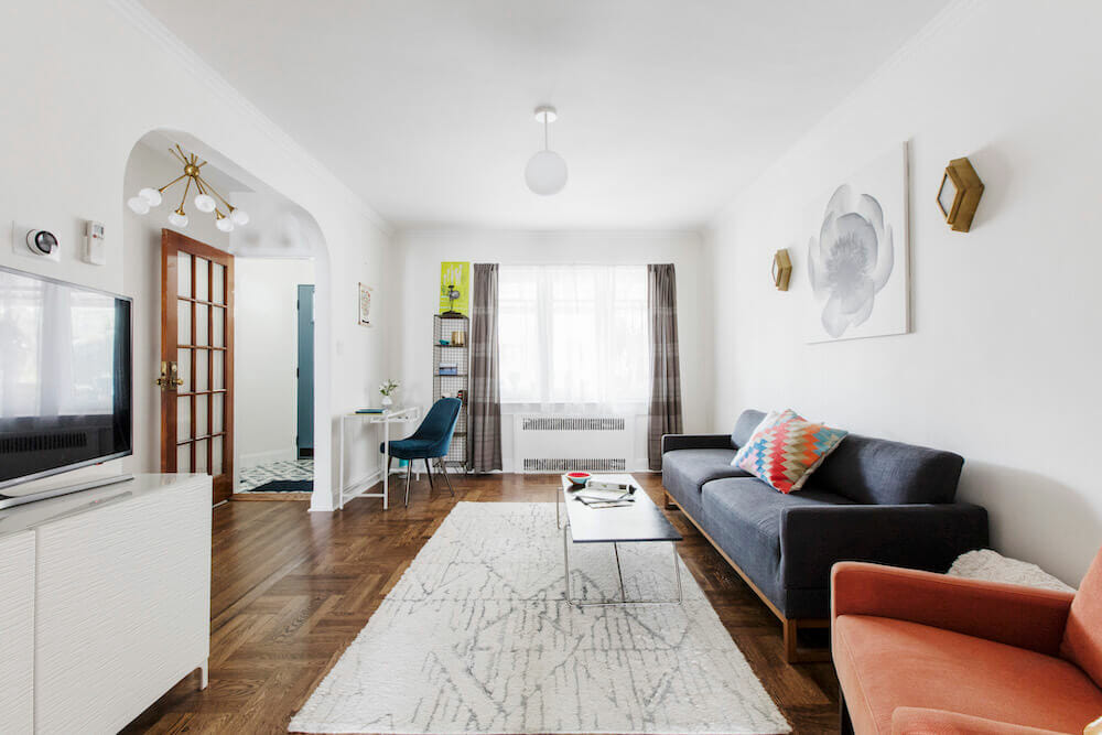 salon blanc avec canapé bleu et rouge et tapis de sol blanc sur parquet et grande fenêtre après rénovation