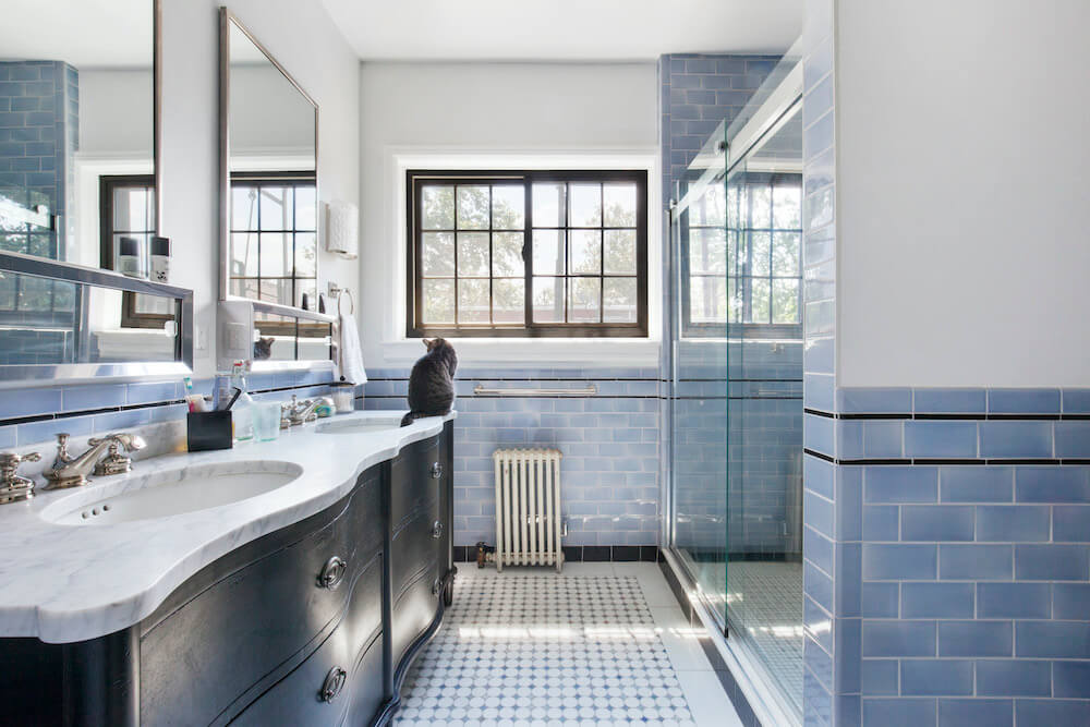 Salle de bain bleue et blanche avec long lavabo double et porte de douche en verre après rénovation